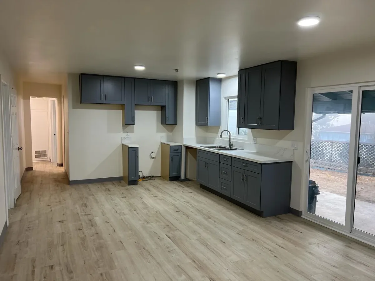 Almost-complete kitchen with gray shaker cabinets, quartz countertops, and new wood-look flooring in a San Diego remodel.