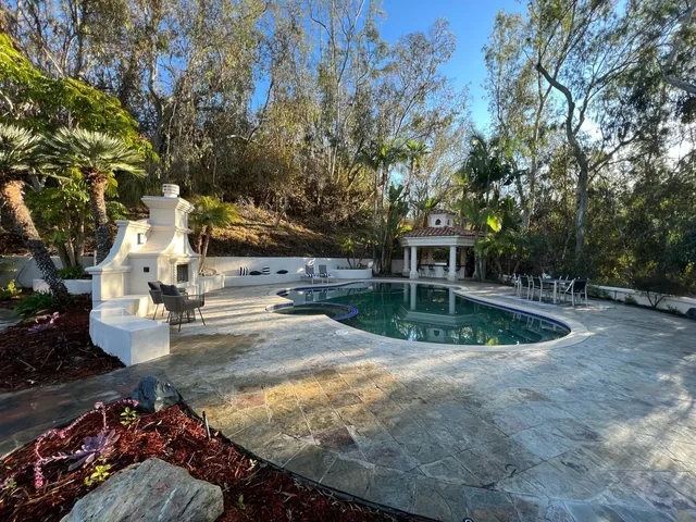 Luxury backyard in San Diego with custom pool, built-in outdoor fireplace, gazebo bar, and stamped concrete decking surrounded by mature landscaping.