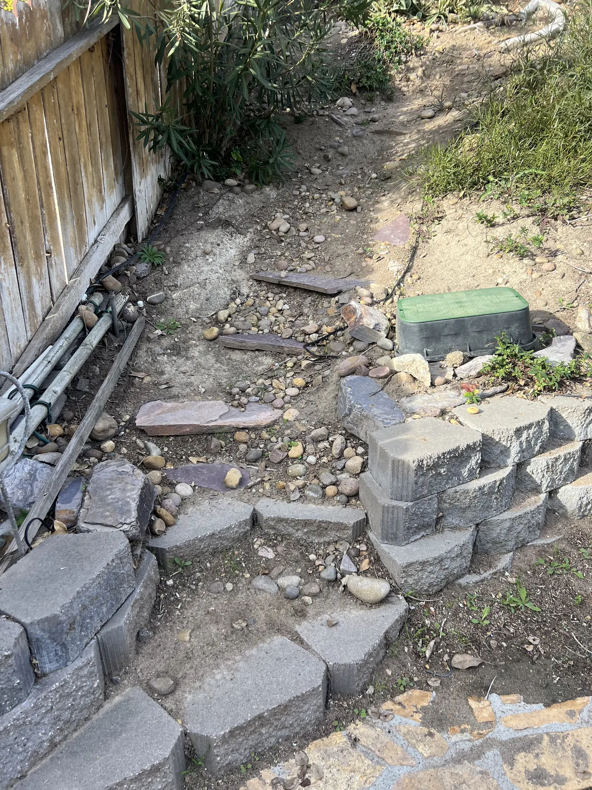 Backyard slope before the work: a collapsed block retaining wall, loose stones and bare soil