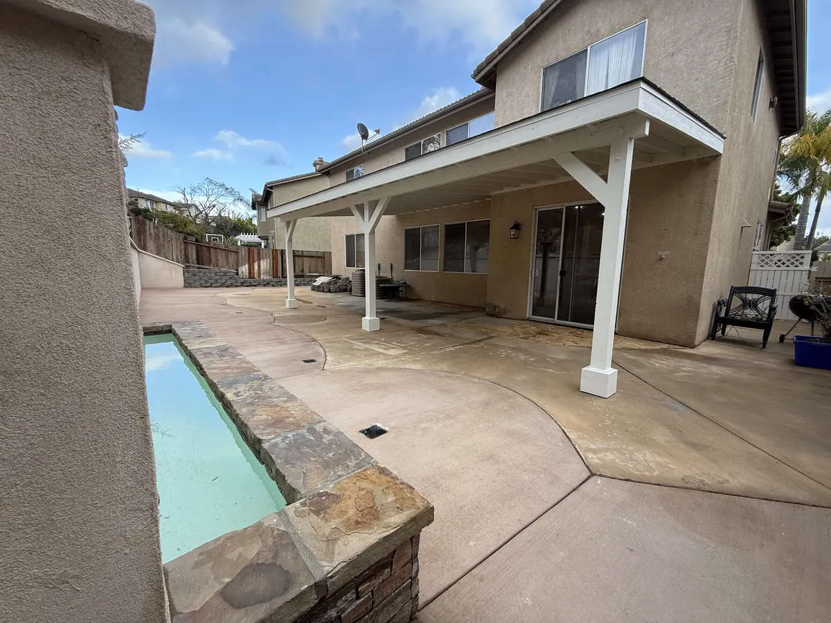 Backyard after the work: a stone-edged water feature basin in front of the existing white patio cover