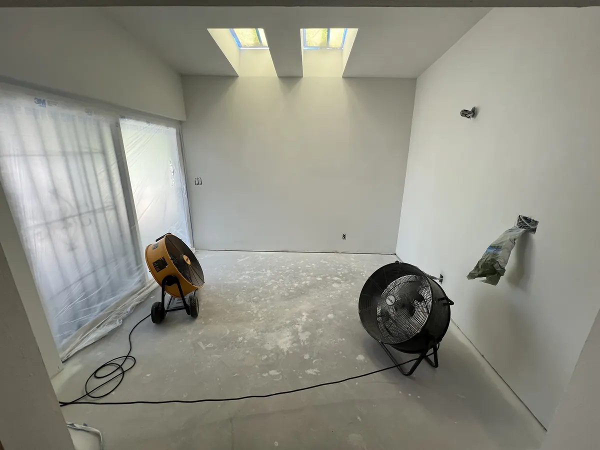 Room with the bare concrete slab exposed and fans drying it before the new flooring
