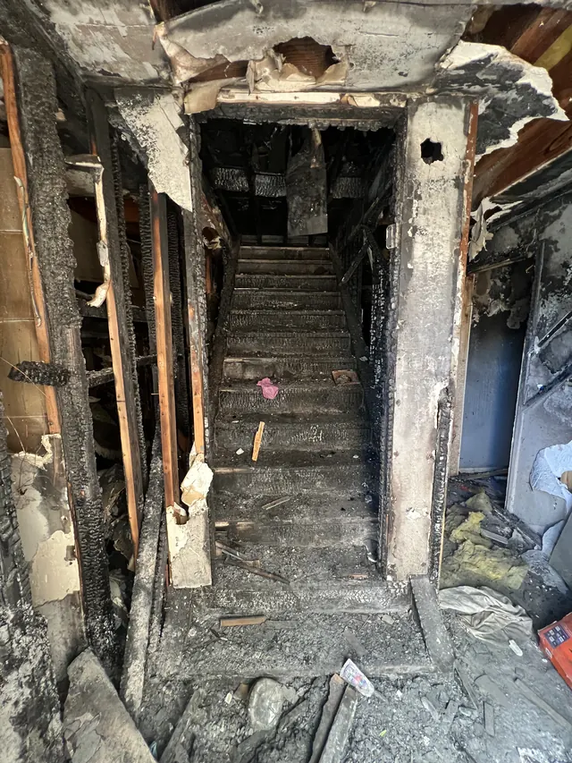 Interior staircase after a house fire, with charred treads, burnt wall framing and debris
