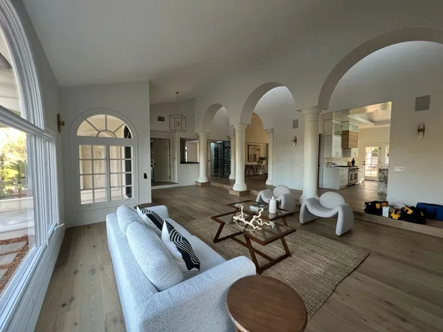 Spacious living room with white columns and arches, modern seating on a rug, and large windows.