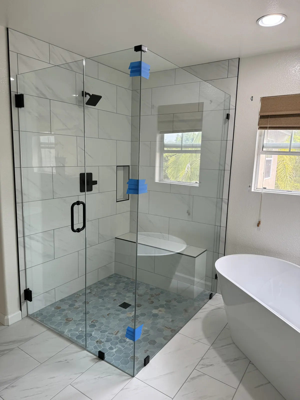 Frameless glass corner shower with a bench and hexagon mosaic floor beside a freestanding tub