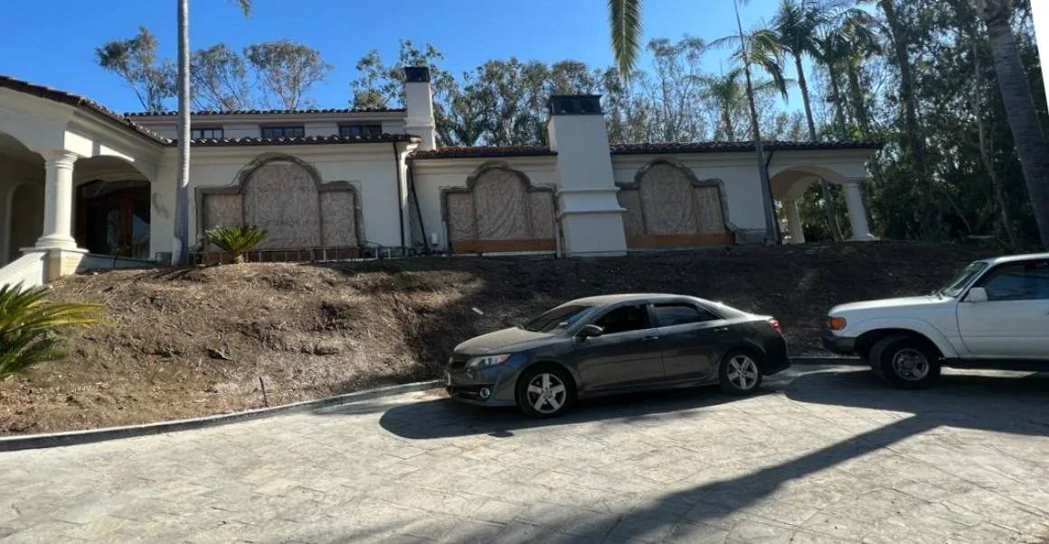 Mediterranean San Diego home before renovation, with boarded windows and bare hillside