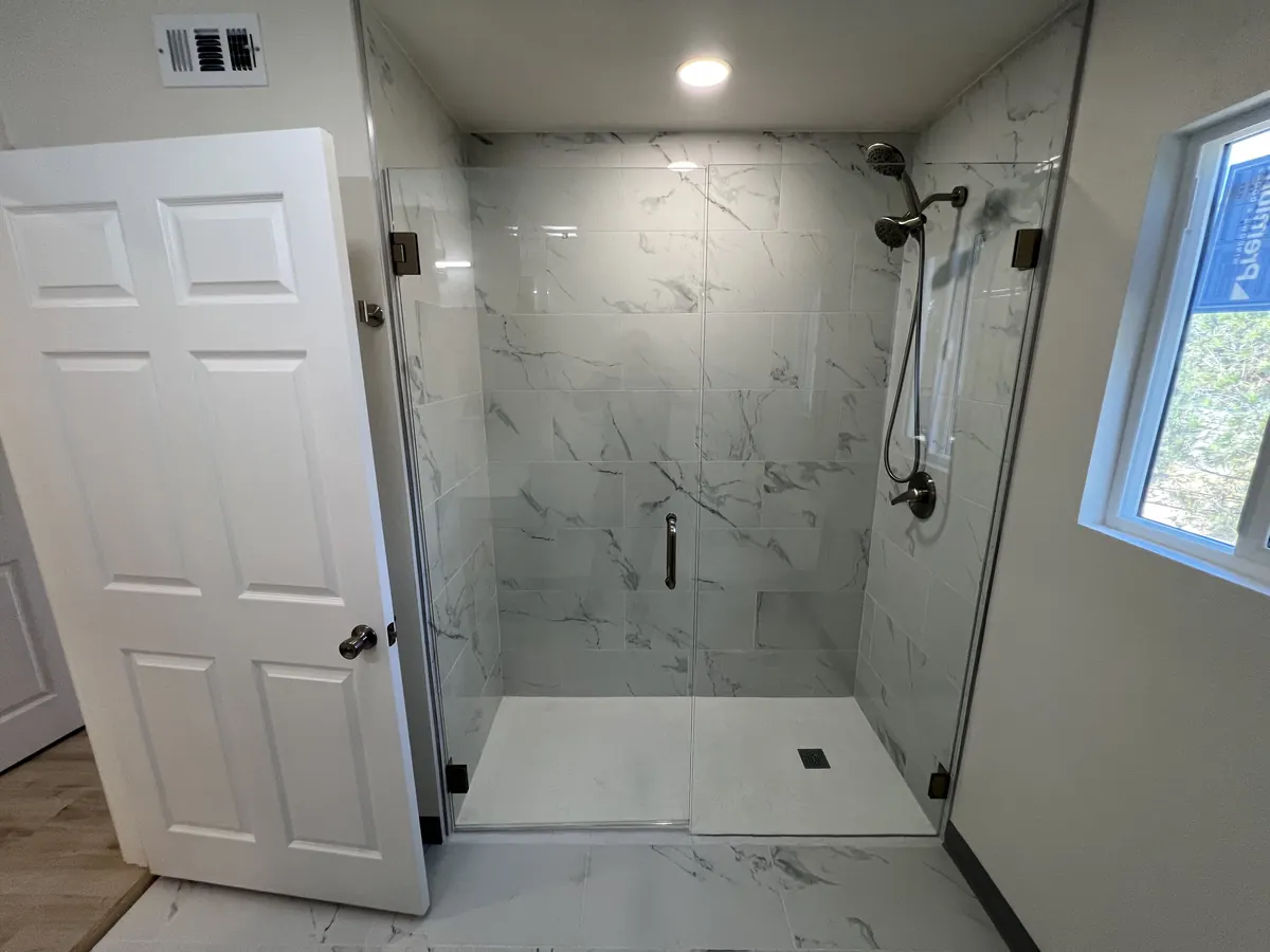 Rebuilt bathroom with a marble-look tile shower, frameless glass panel and black shower fixtures