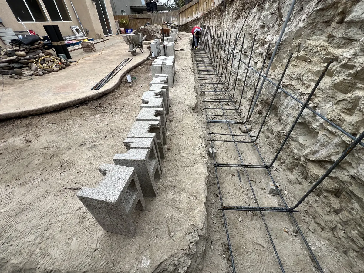 Vertical rebar along the slope with hollow concrete blocks staged for the retaining wall
