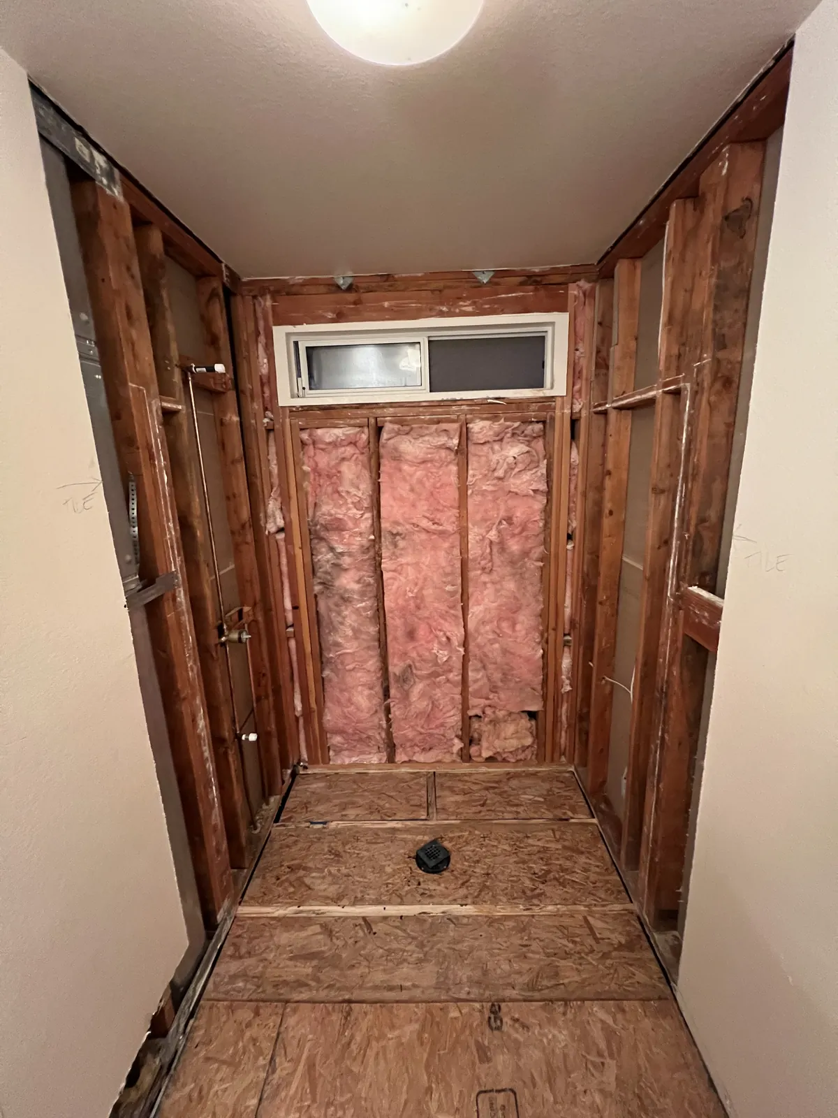 Tub and shower area stripped to the studs, insulation and drain exposed, ready for the new shower