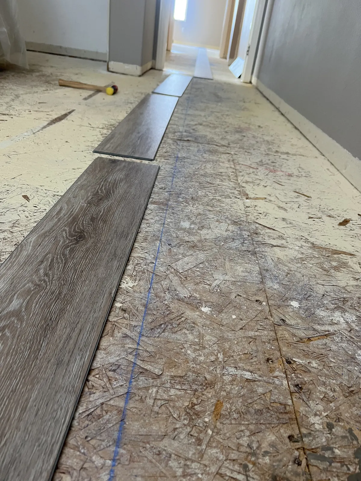 First rows of vinyl plank laid over the prepared plywood subfloor along a chalk line