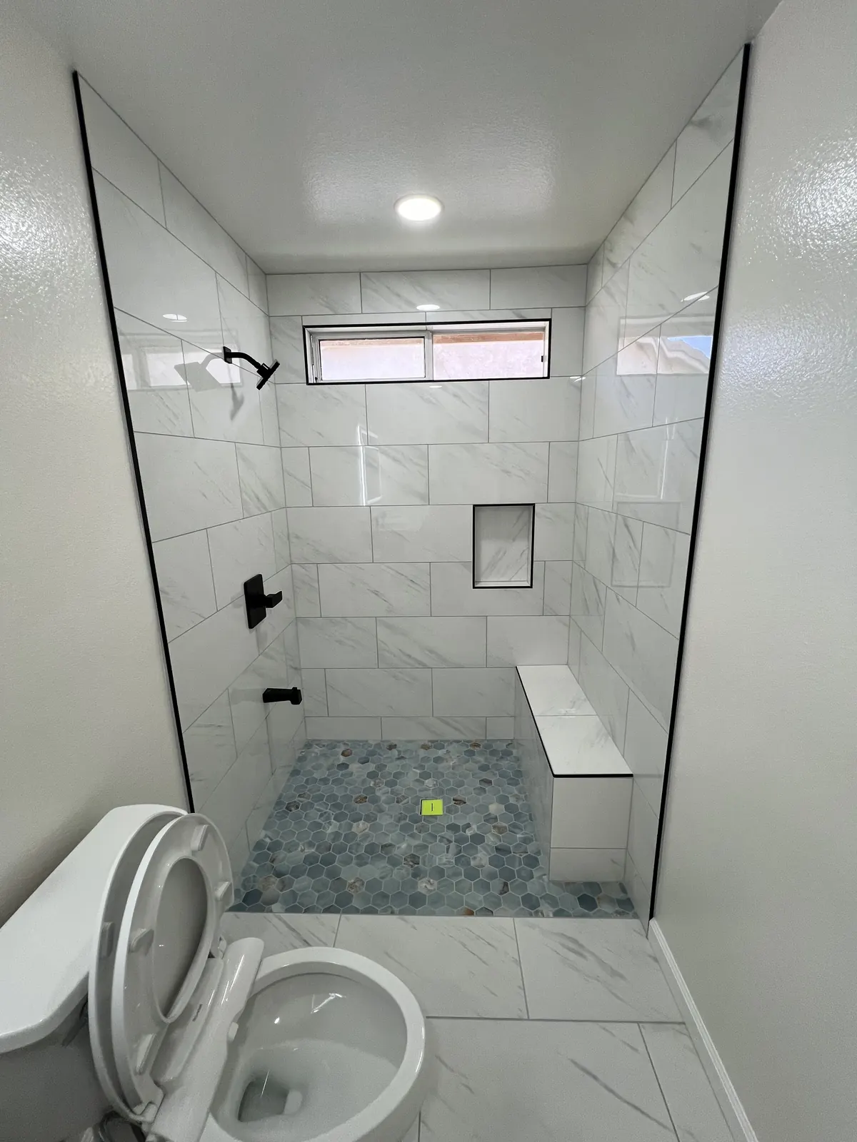 Finished walk-in shower with marble-look tile, a bench, a recessed niche and a hexagon mosaic floor