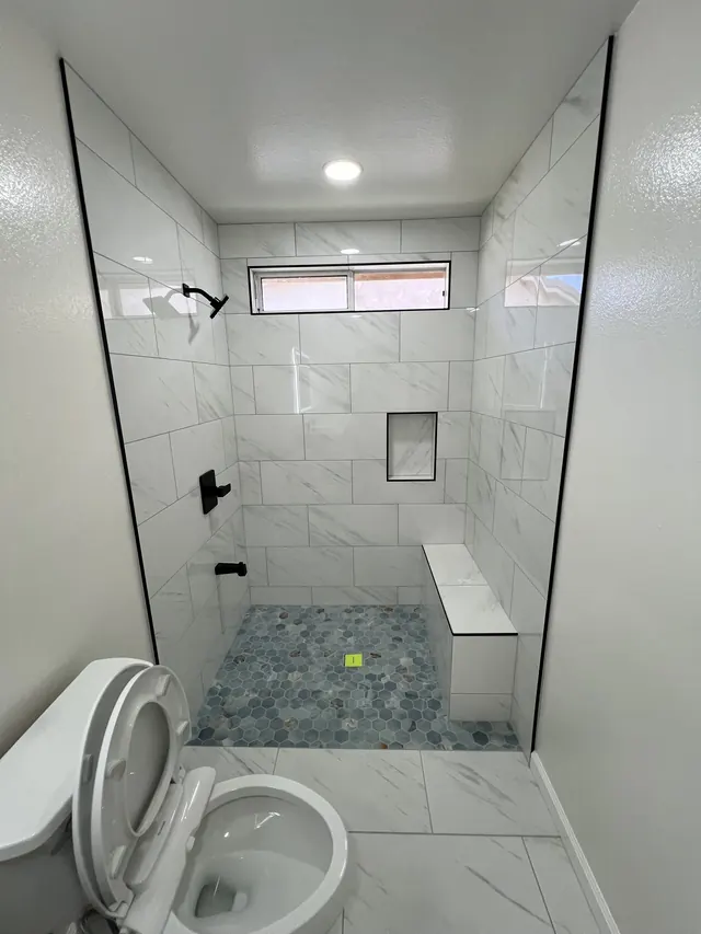 Finished walk-in shower with marble-look tile, a bench, a recessed niche and a hexagon mosaic floor