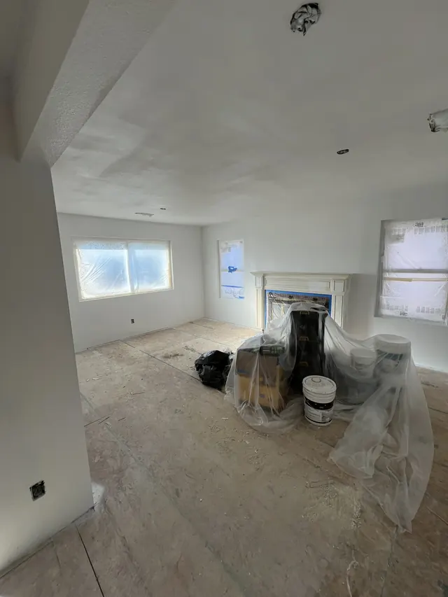 Living room with new drywall and a fireplace surround, floor protected before the final finishes