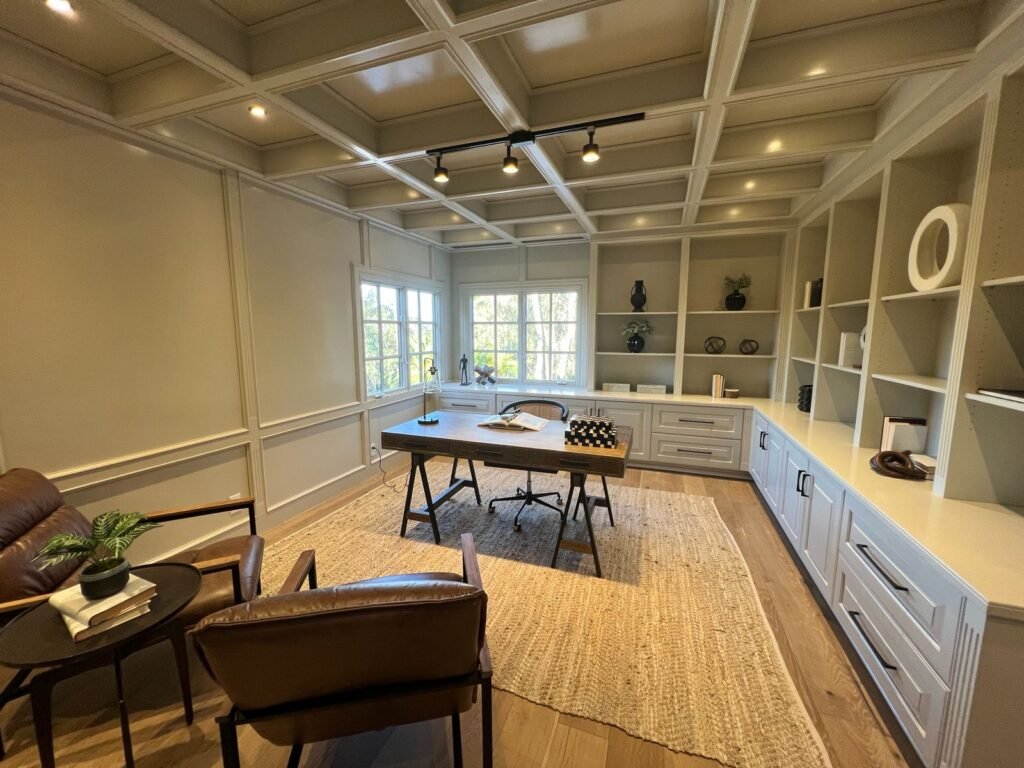 Finished home office with coffered ceiling, built-in shelving and cabinets, wood desk, and lounge seating over hardwood floors