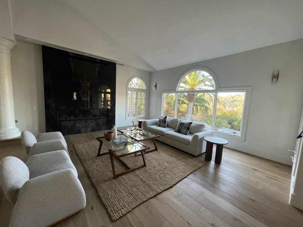 Bright living room with large arched windows, light wood floors, neutral seating, and a sleek black fireplace wall