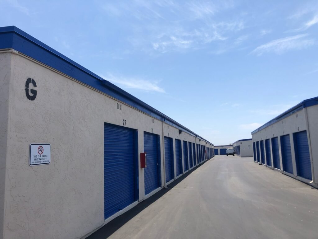 Row of beige stucco storage units with blue roll-up doors under a clear sky — Construction Crafters project.