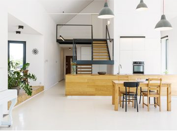 A bright modern open-plan interior with a wooden kitchen island, dining table, and loft staircase. home remodeling