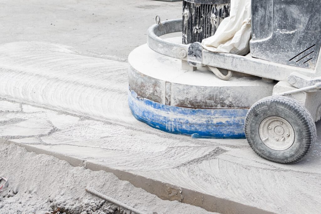 Close-up of a floor grinding machine smoothing a concrete surface, with dust and swirl marks visible — Construction Crafters home remodeling