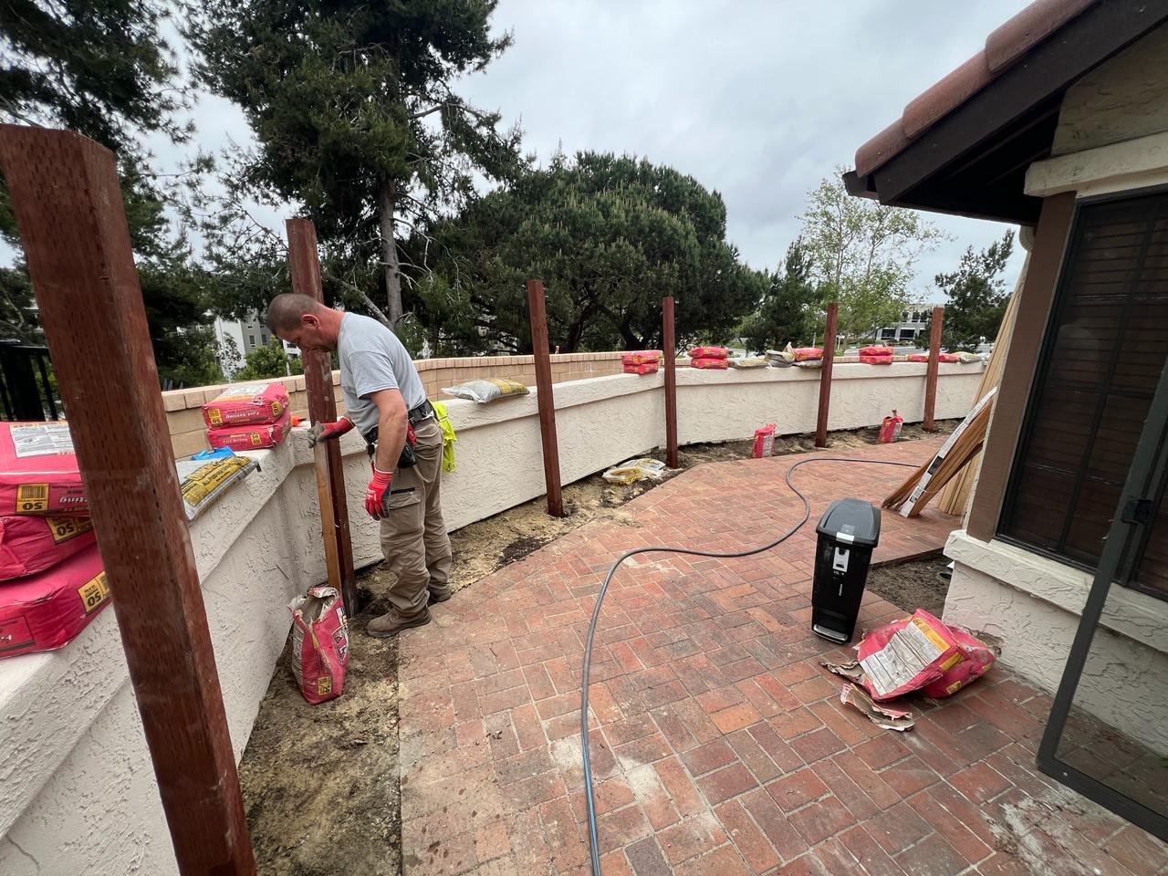 Construction worker setting vertical wood posts along a brick patio edge in a San Diego backyard renovation