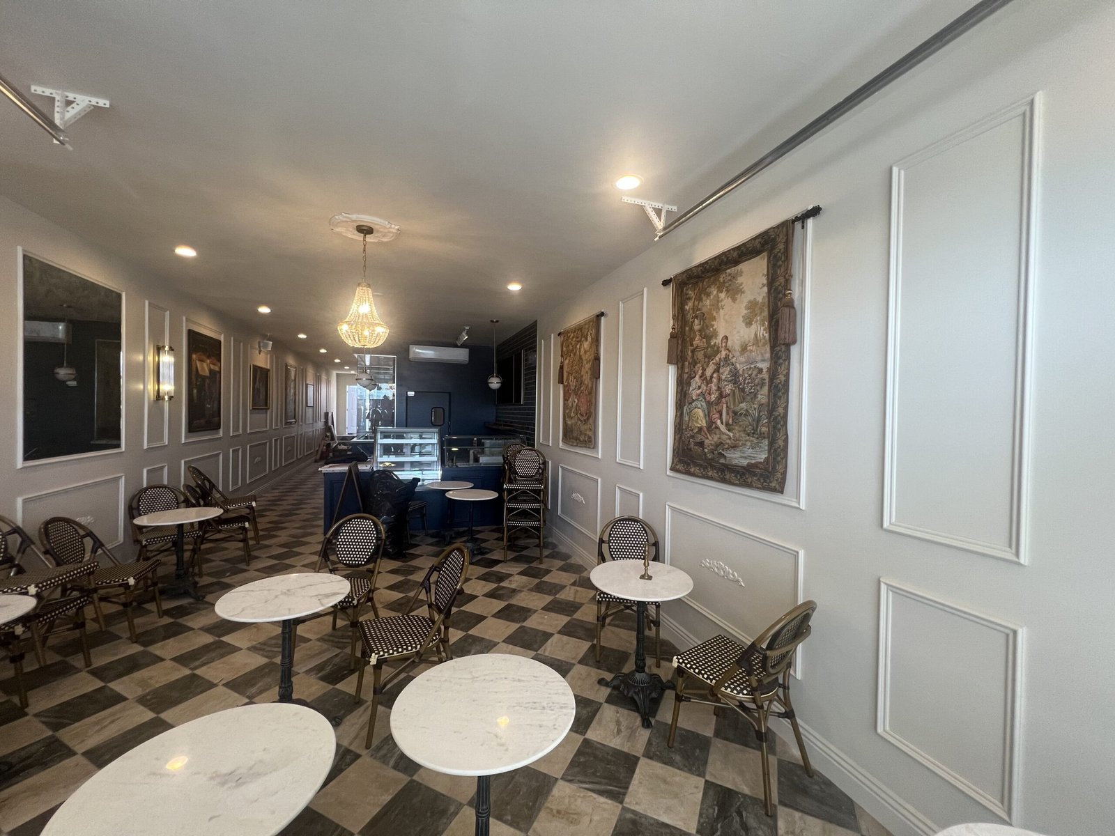 Finished upscale commercial interior with marble-topped bistro tables, decorative wall paneling, and chandelier lighting.