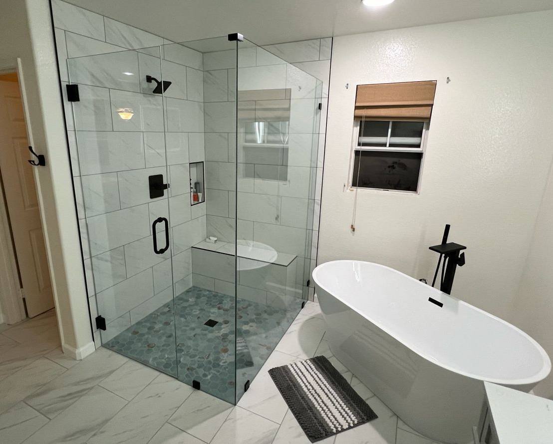 Contemporary bathroom with glass-enclosed marble-tile shower, pebble floor accent, and freestanding tub under recessed lighting.