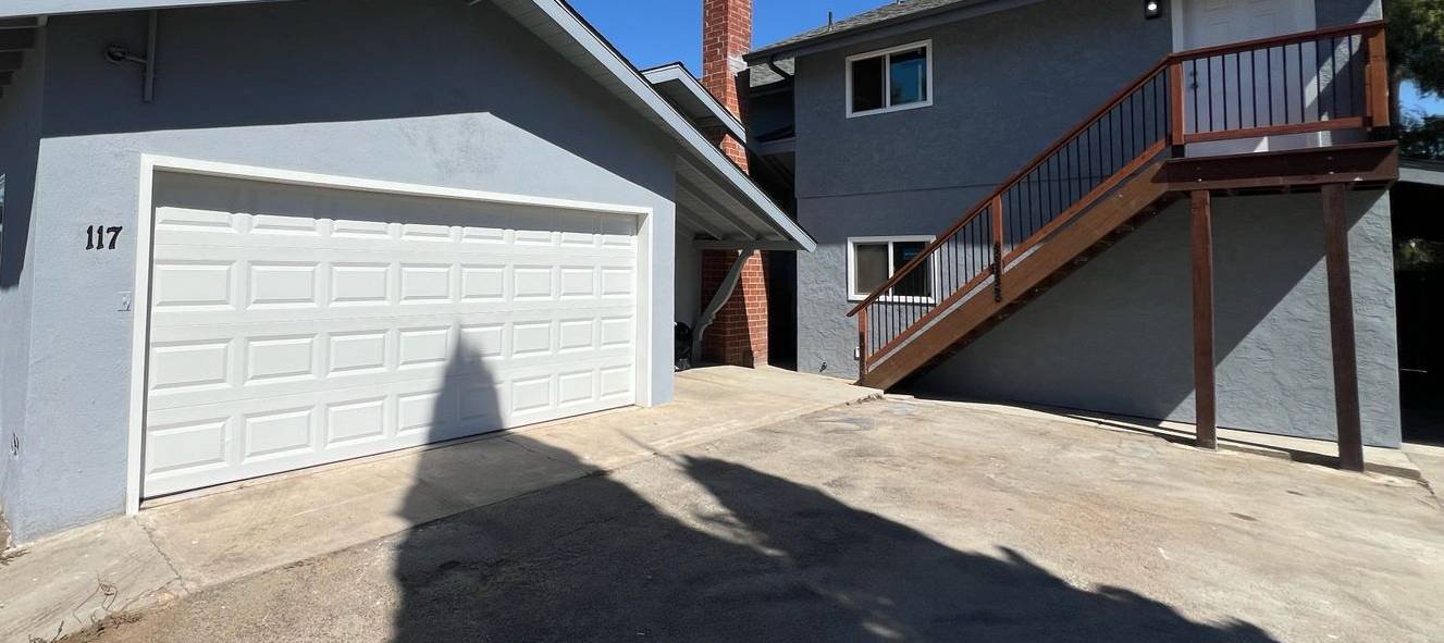 Updated two-story San Diego home with fresh gray stucco, new exterior staircase with wood and metal railing, and clean white garage door.