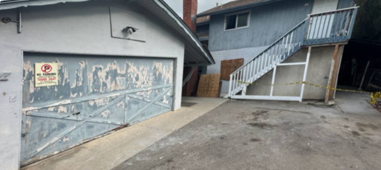 Weathered two-story San Diego home with peeling paint on the garage door and exterior staircase leading to upper level.
