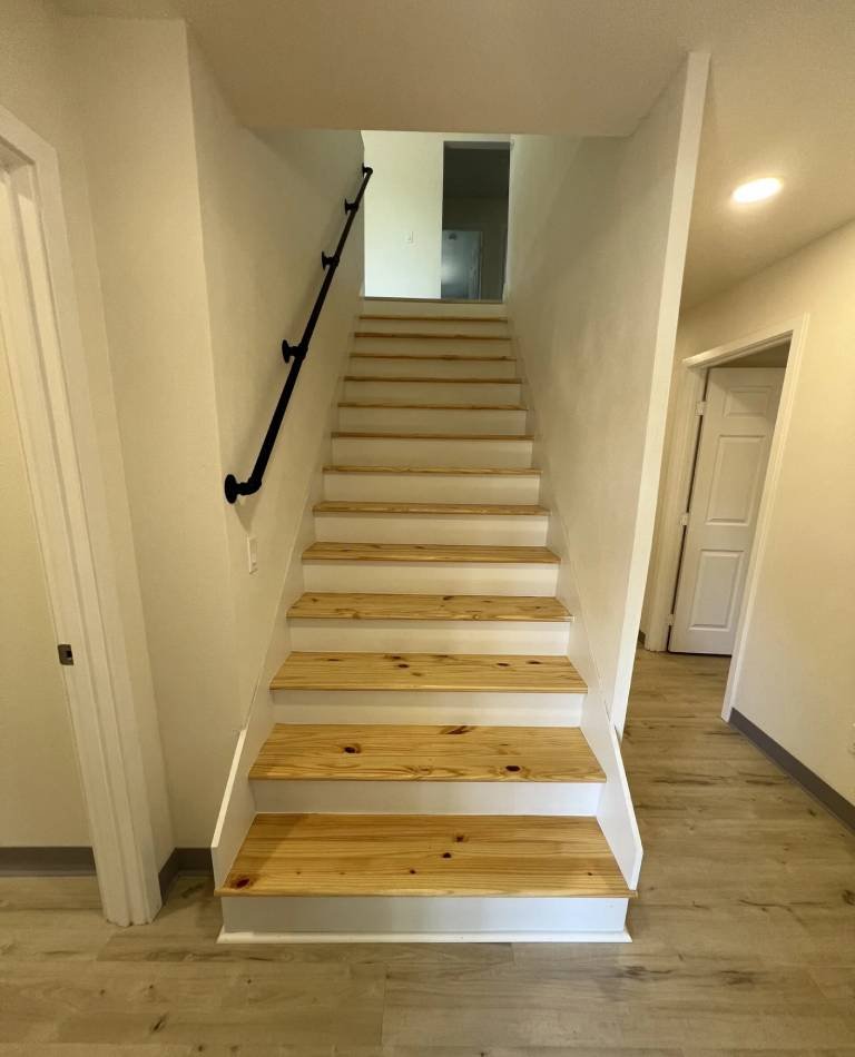 Interior staircase with natural wood treads, white risers, a matte-black handrail, and light vinyl plank flooring