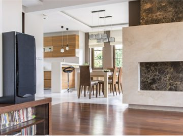 Open-concept living and dining area with a modern fireplace, wood and tile floors, and a kitchen with wood cabinets — Construction Crafters home remodeling