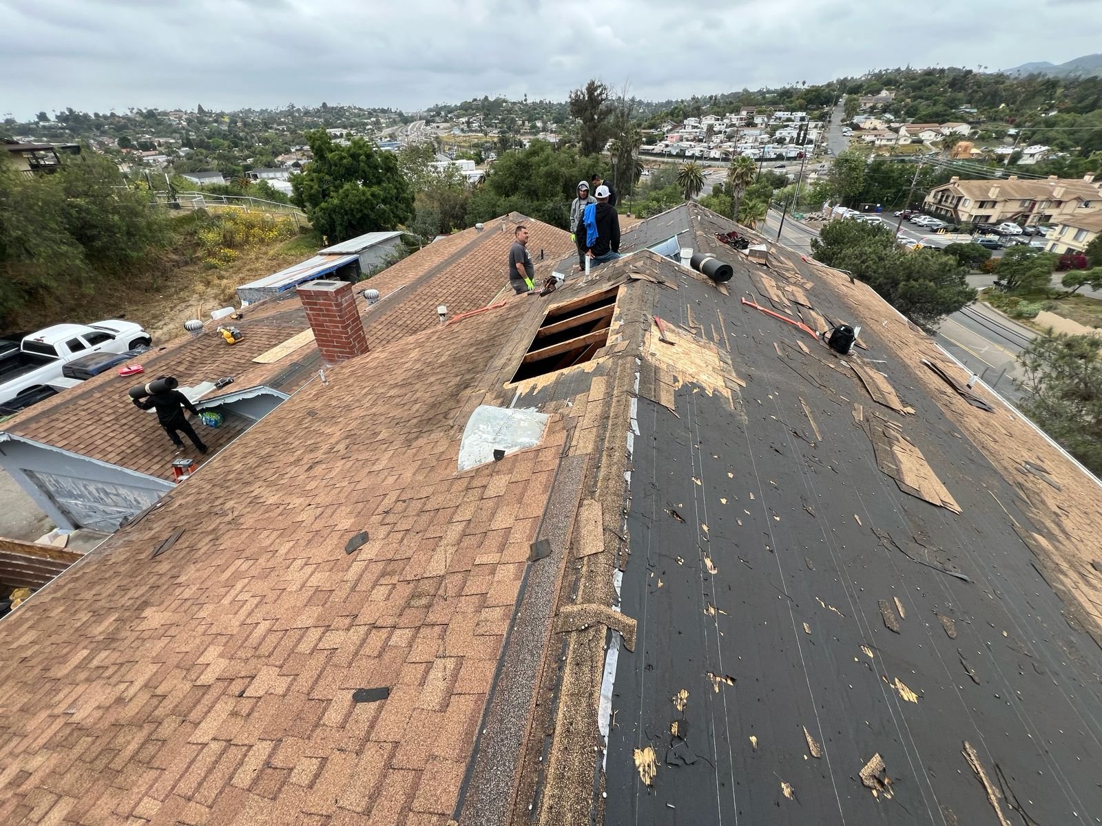 Roofing crew on a sloped residential roof in San Diego removing old shingles and preparing decking for replacement.