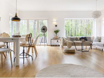 This bright open-plan dining and living area with light wood floors, white walls, large windows, and modern furnishings — Construction Crafters home remodeling