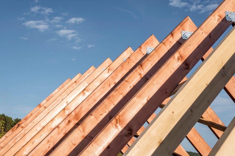 Wooden roof rafters with metal connector plates against a blue sky — Construction Crafters home remodeling
